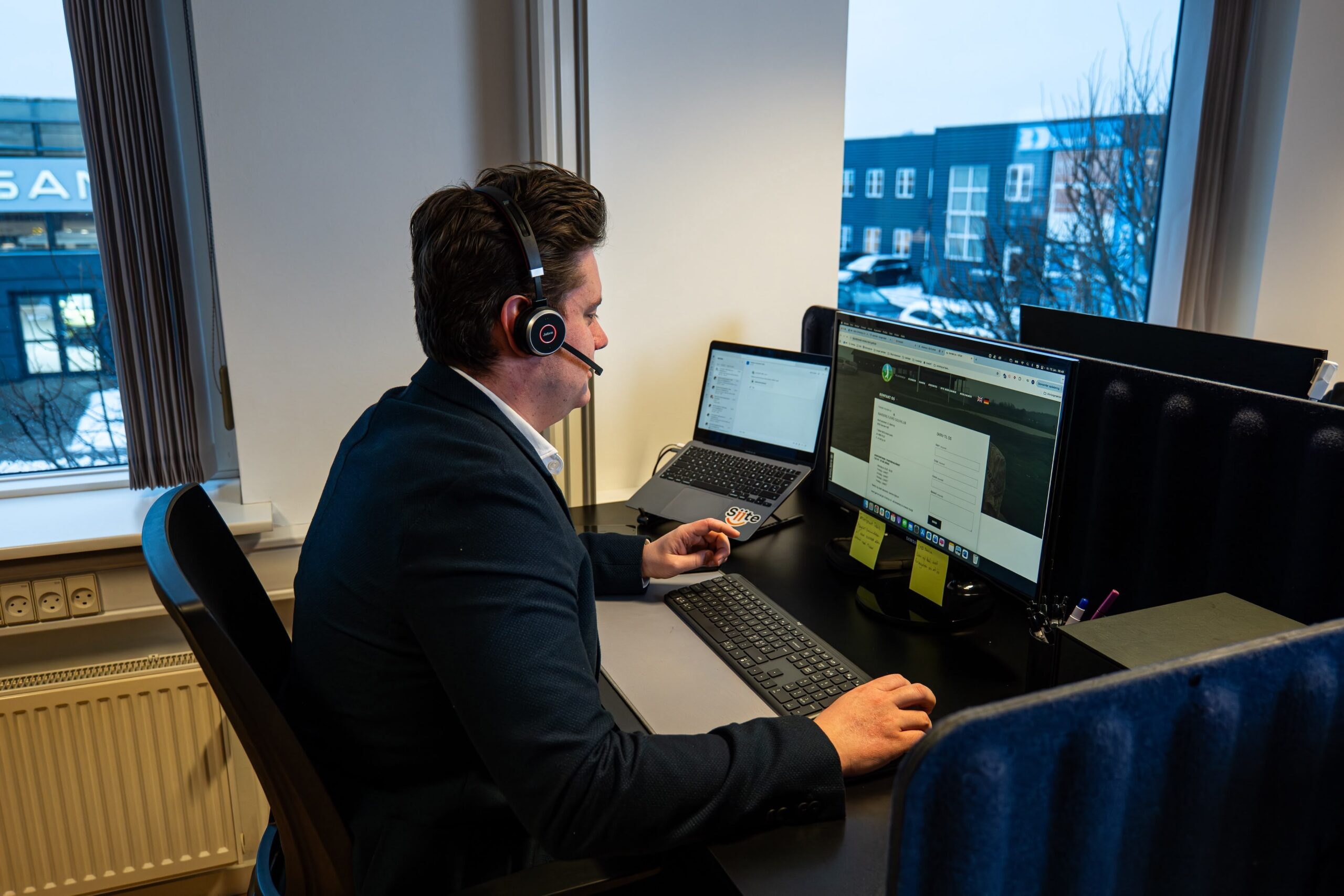 Osoba radi na računaru sa slušalicama na glavi u uredu.